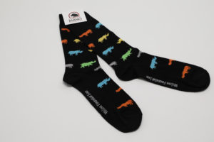A pair of super-soft black socks with green, grey, blue, yellow , and orange Rhinos on them. Along the sole of the sock is their branding as well as on the packaging that comes with it.
