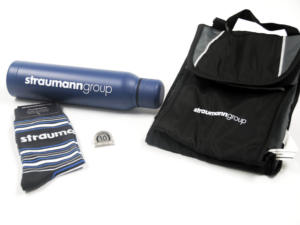 A pair of socks, a lunchbag cooler, an insulated waterbottle, and a pin all designed and produced with Straumann Group branding.